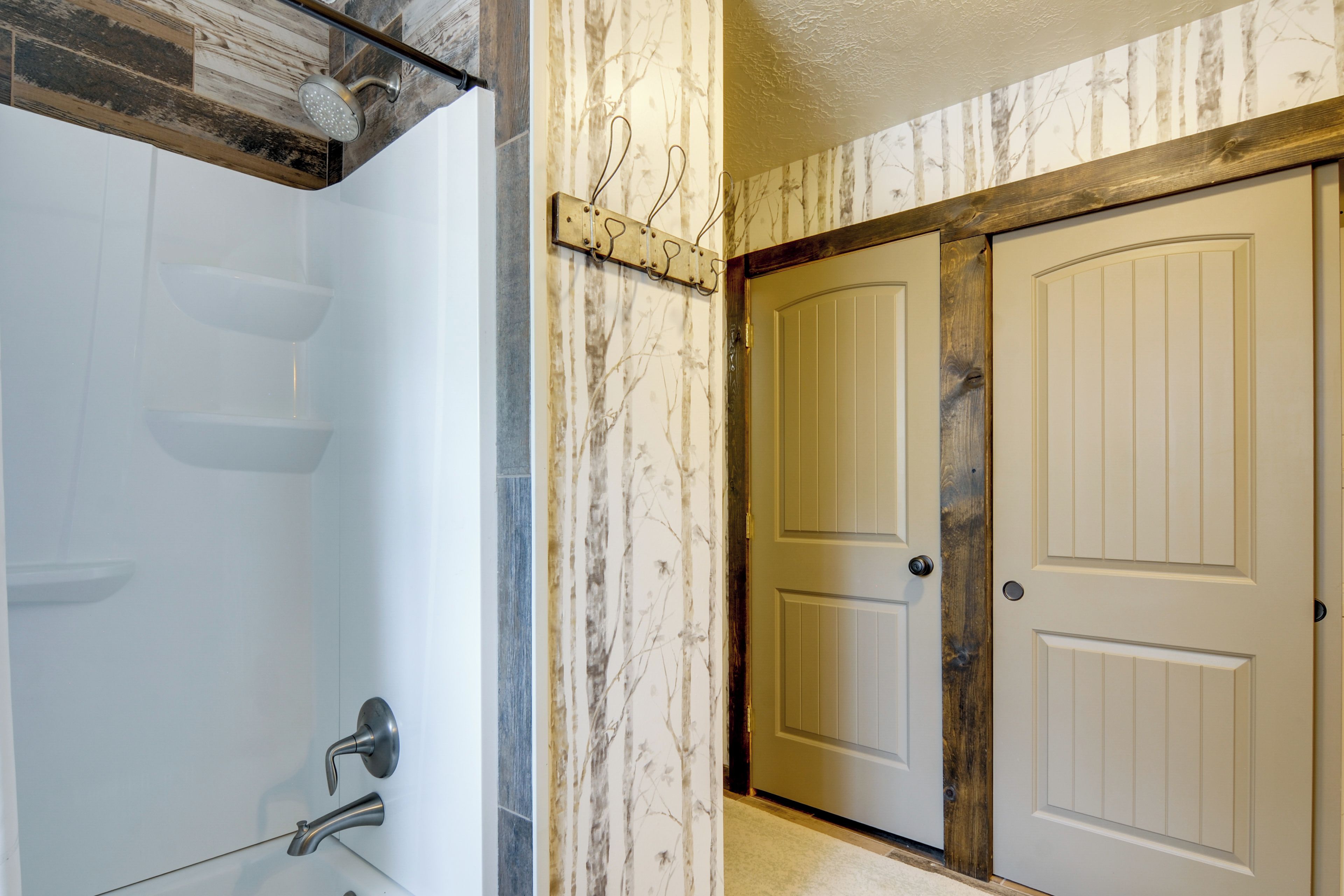 A bathroom with a shower, a toilet, and a sink. There is a wooden door and a wall with a tree pattern.