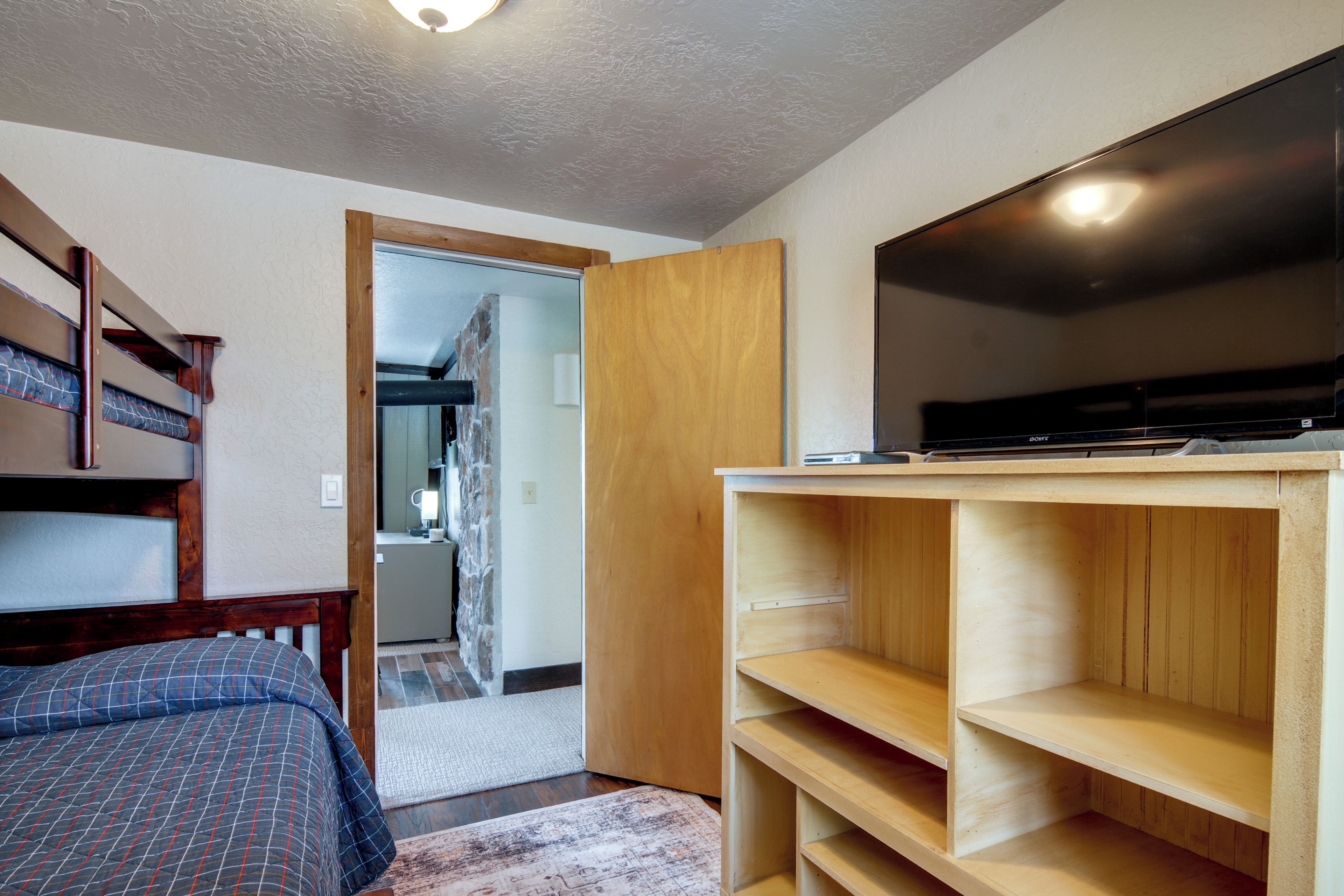 Un dormitorio con cama, televisor, estanterías de madera y armario.