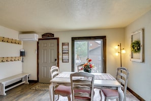 A dining area with a table, chairs, and a bench. There is a door with a sign above it, a wall-mounted air conditioner, and a wall-mounted light fixture.