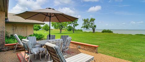 An outdoor patio with a table and chairs, a large umbrella, and a view of a lake.