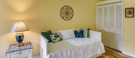 A bedroom with a bed, bedside table, lamp, decorative wall piece, closet, and a window.