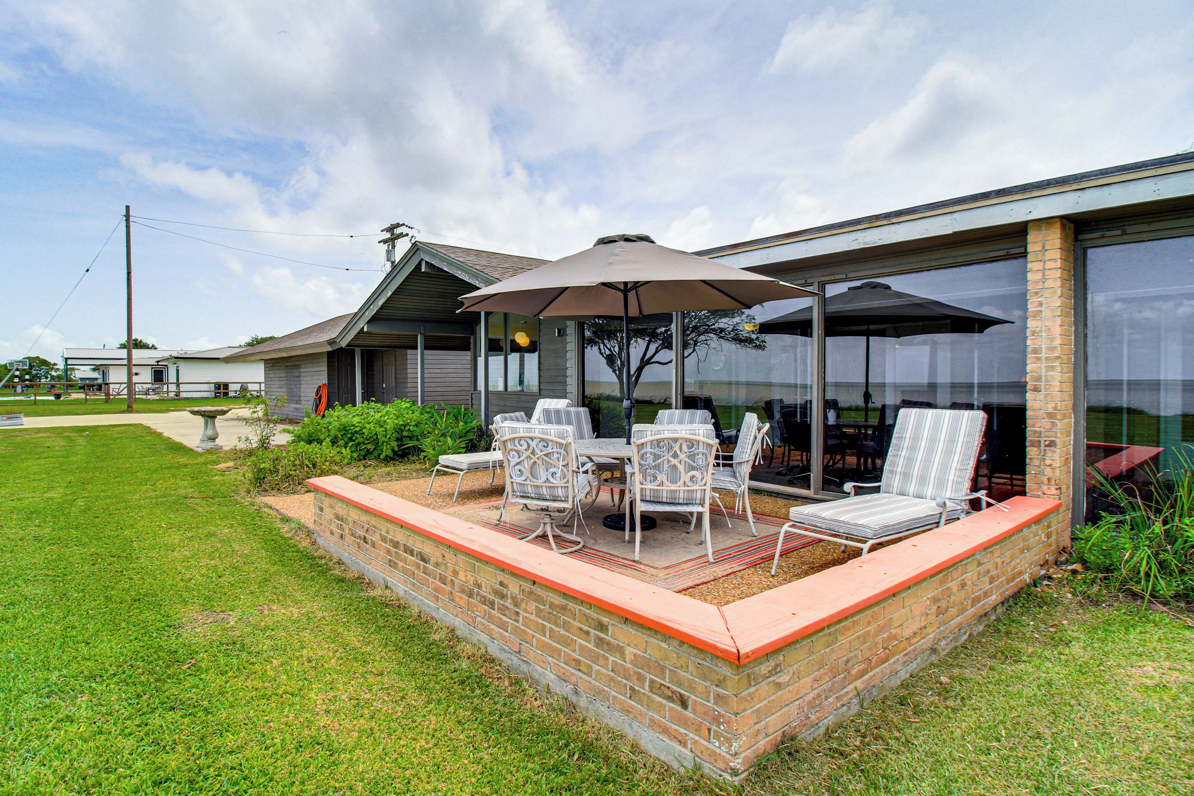 An outdoor patio with a brick wall, a table, chairs, and a large umbrella.