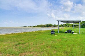 A grassy area with a water body, a covered seating area, and a trash bin.