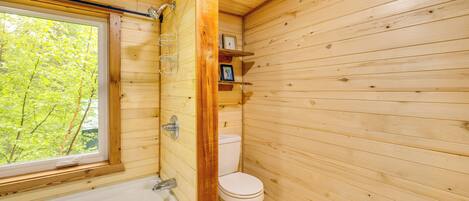 A wooden cabin bathroom with a window, a bathtub, and a toilet.