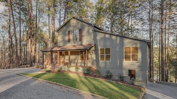 A two-story house with a porch, surrounded by a forest.