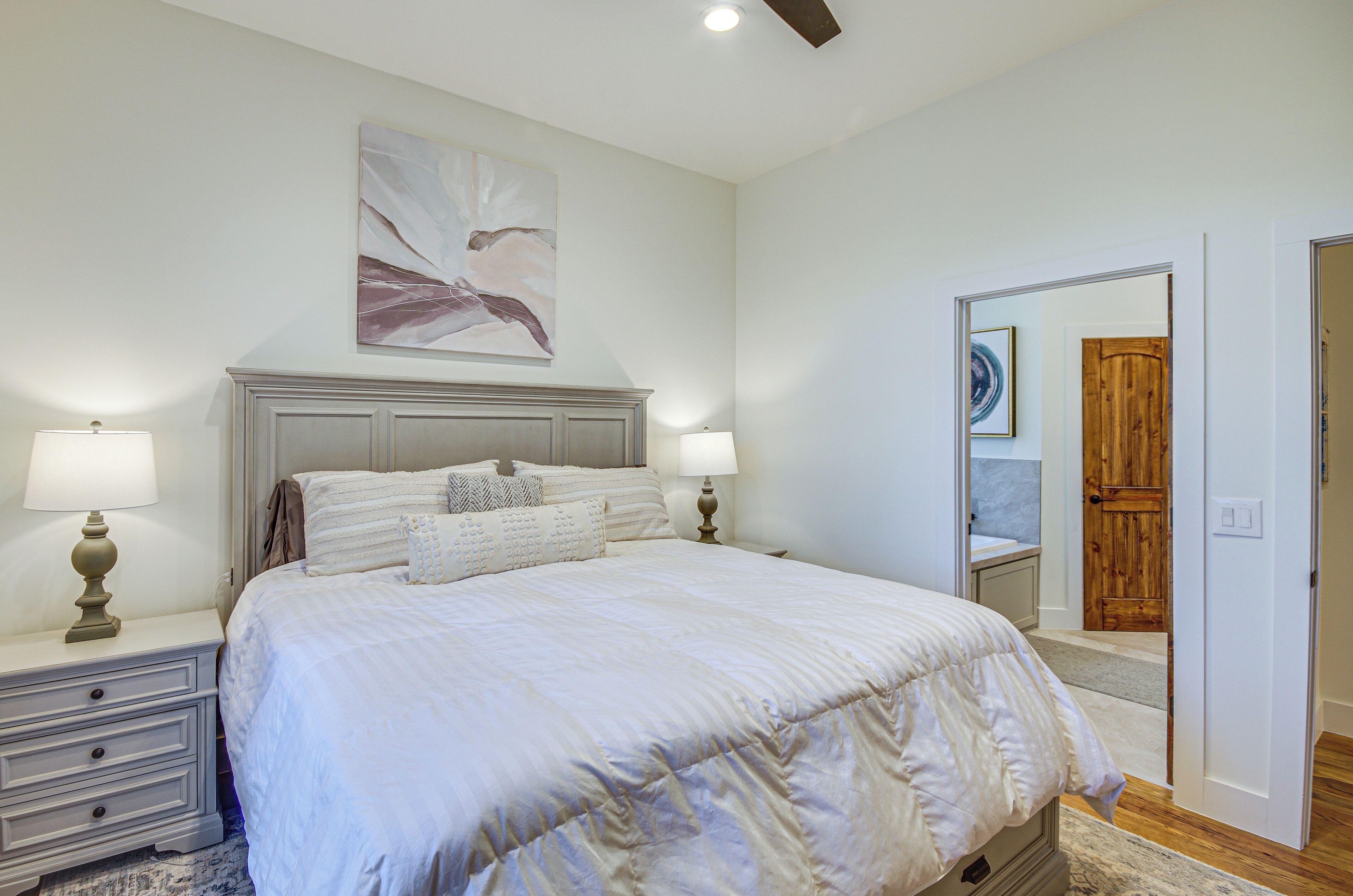 A bedroom with a large bed, two bedside tables with lamps, a wooden door, and a mirror.