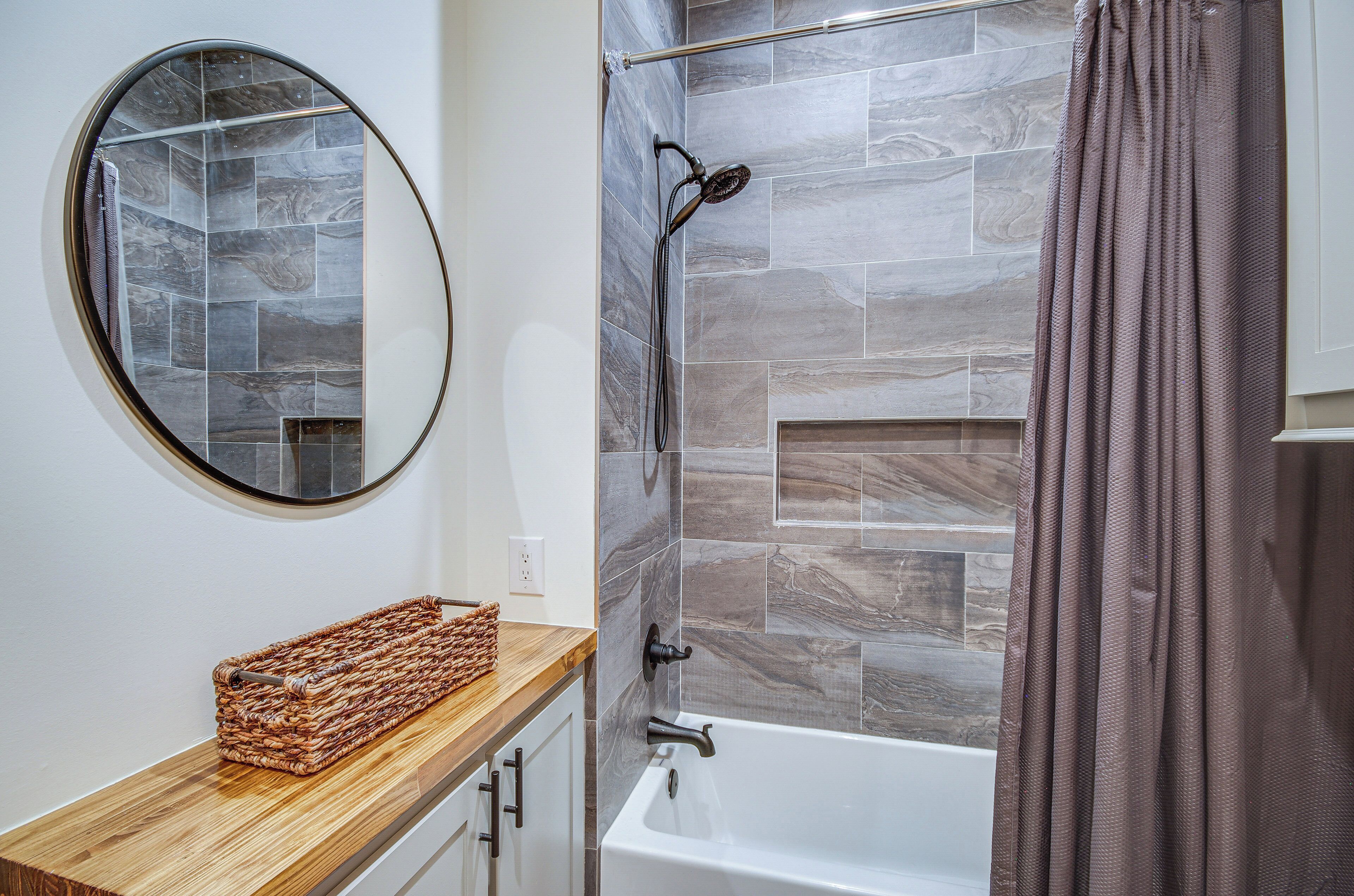 A bathroom with a shower, a round mirror, a wooden vanity, and a towel rack.