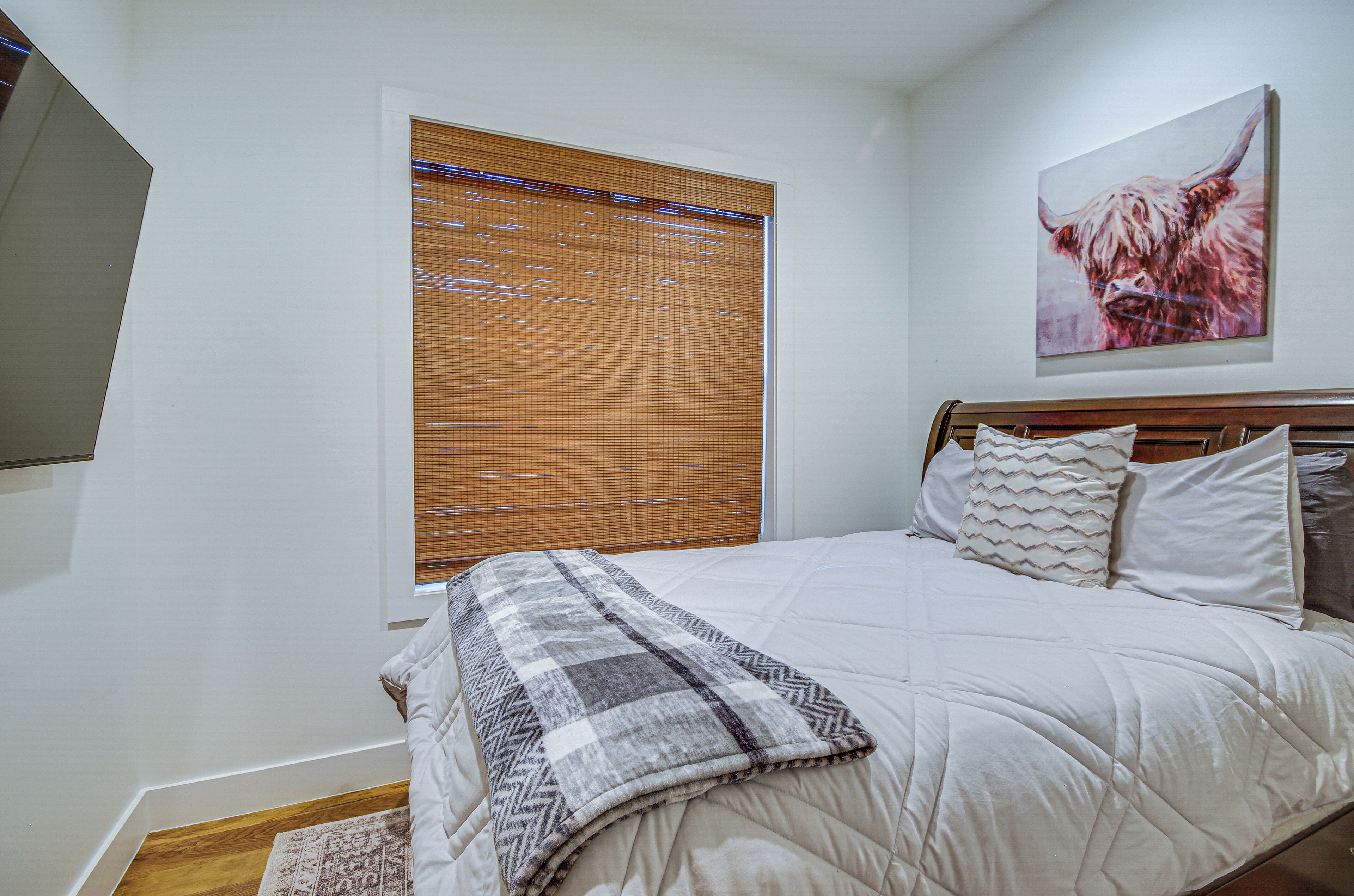 Un dormitorio con cama, ventana con persianas, un cuadro en la pared y cabecera de madera.