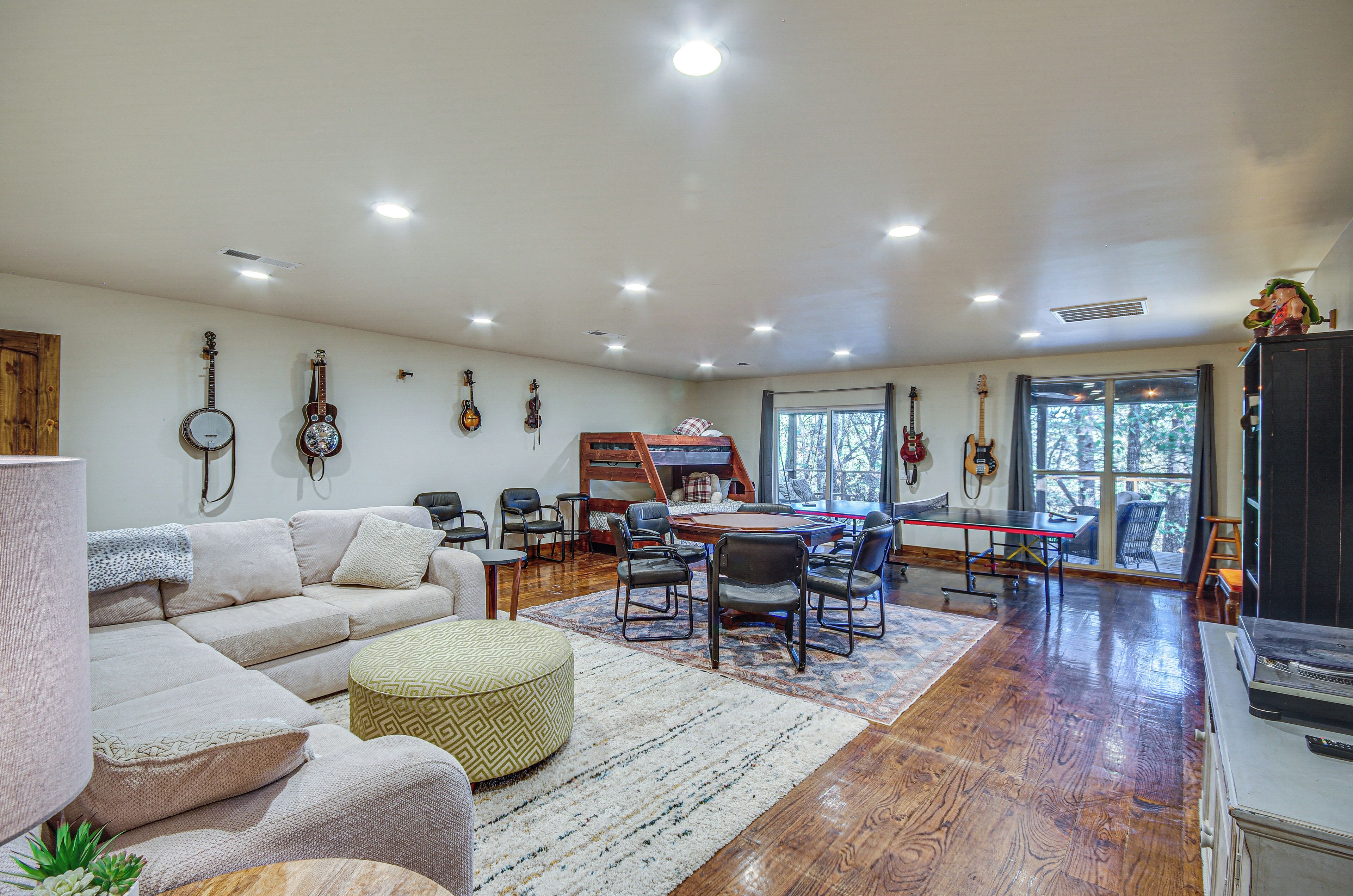 A spacious living room with a large sofa, a dining table, and several chairs. There are guitars hanging on the wall and a piano in the corner.