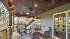 Eine überdachte Terrasse im Freien mit Rattanmöbeln, einem Deckenventilator und Blick ins Waldgebiet.