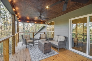A covered outdoor deck with wicker furniture, a ceiling fan, and a view of the forest. - Waterfront Home w/ 3 Decks, Fire Pits and Hot Tub! (Terry)