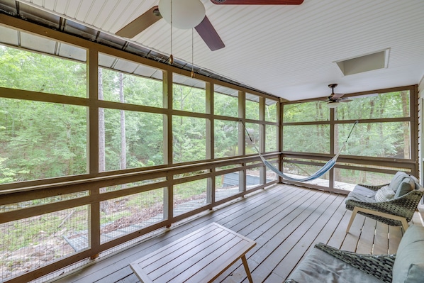 A covered porch with large windows, a hammock, and a wicker chair. - Off-grid Creekside Cabin Near Lake Jordan (Titus)