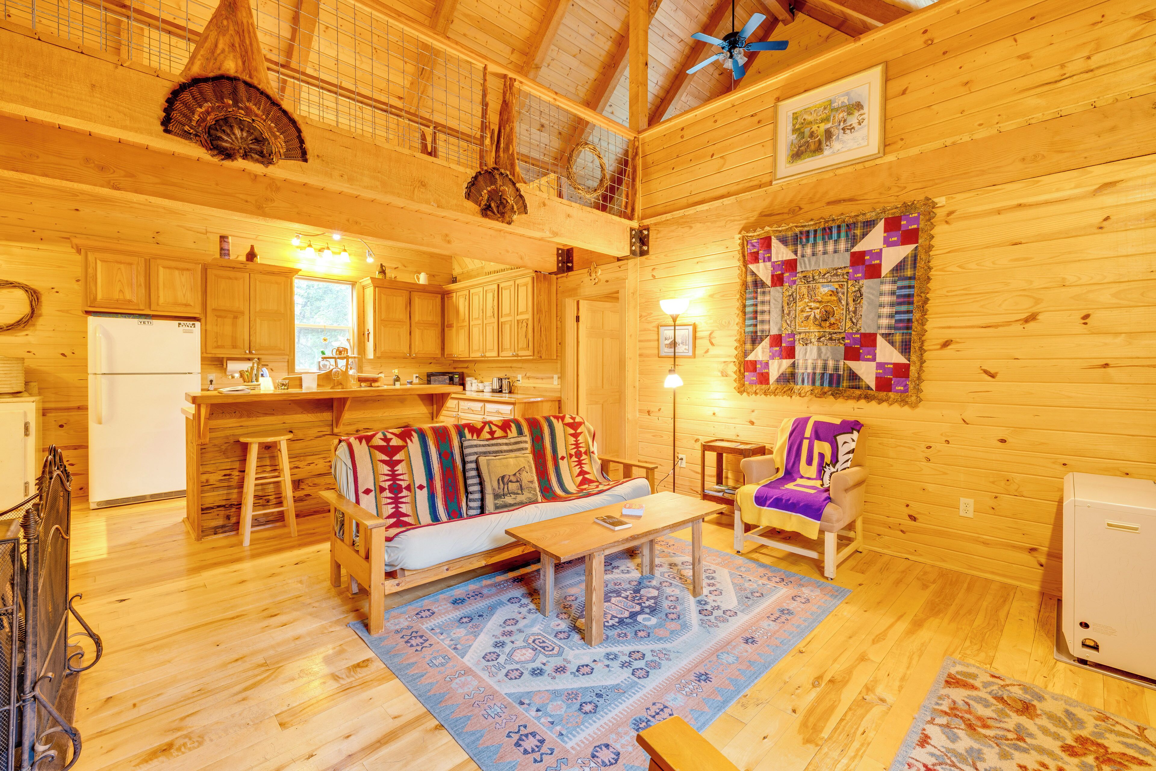 A cozy log cabin interior with a kitchen, dining area, and living room furnished with a sofa, armchairs, and a coffee table.