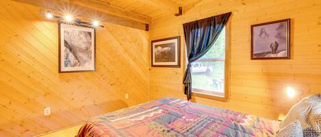 Une pièce de style cabane en bois, avec un lit, des tableaux encadrés aux murs et une fenêtre avec des rideaux.