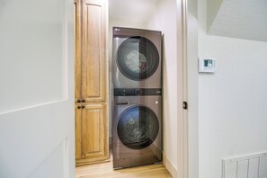 A laundry room with a front-loading washer and dryer, wooden cabinets, and a thermostat on the wall. - Lake Views, Big Deck, Hot Tub, Fire Pit, Game Room (Park Hill)