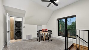 A room with a ceiling fan, a dining table with chairs, a washer and dryer, and a large window with a view of trees. - Lake Views, Big Deck, Hot Tub, Fire Pit, Game Room (Park Hill)
