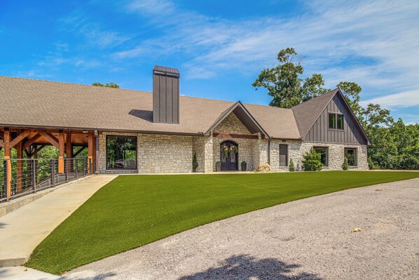 A large stone building with a covered porch, a well-maintained lawn, and a gravel driveway. - Lake Views, Big Deck, Hot Tub, Fire Pit, Game Room (Park Hill)