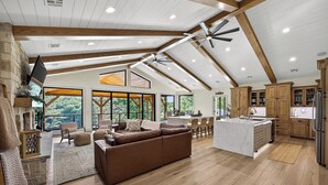 A spacious living area with a large brown sofa, a kitchen with wooden cabinets, and a dining area with a high ceiling and exposed beams. - Lake Views, Big Deck, Hot Tub, Fire Pit, Game Room (Park Hill)
