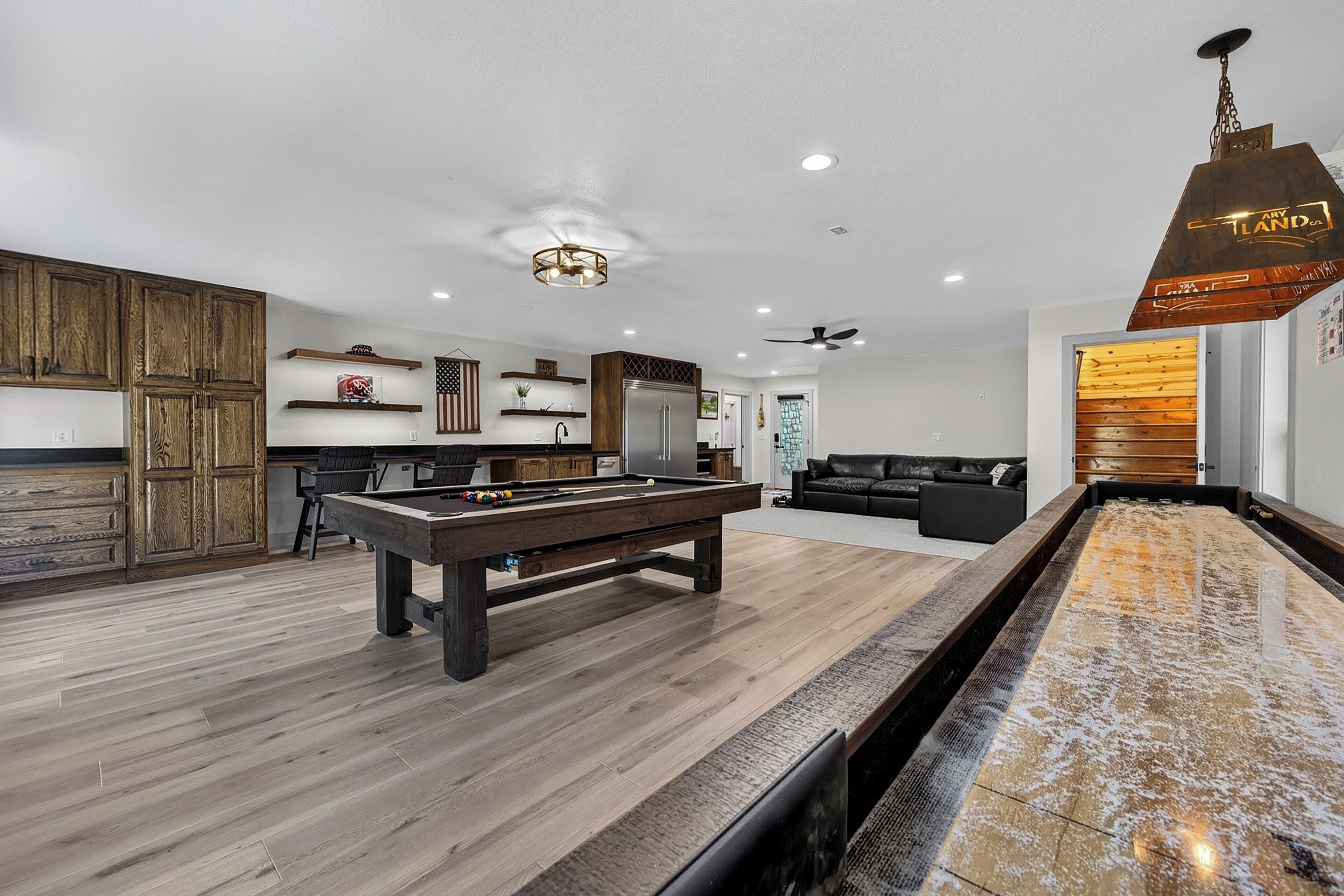 A modern living room with a pool table, wooden cabinets, and a ceiling fan.
