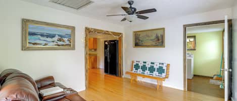 A living room with a brown leather sofa, wooden flooring, a ceiling fan, and two framed paintings.