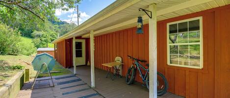 A wooden porch with a bicycle and a table, a window, and a view of a green landscape.