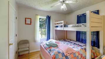 Un dormitorio con literas, una cama individual, una silla, un ventilador de techo y una ventana con cortinas.