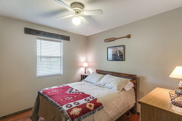 A bedroom with a bed, a nightstand, a wall-mounted lamp, a ceiling fan, a window with blinds, and a wall-mounted picture. - Fishing Pond & Screened Deck 'mourning Dove Lodge' (Alapaha)