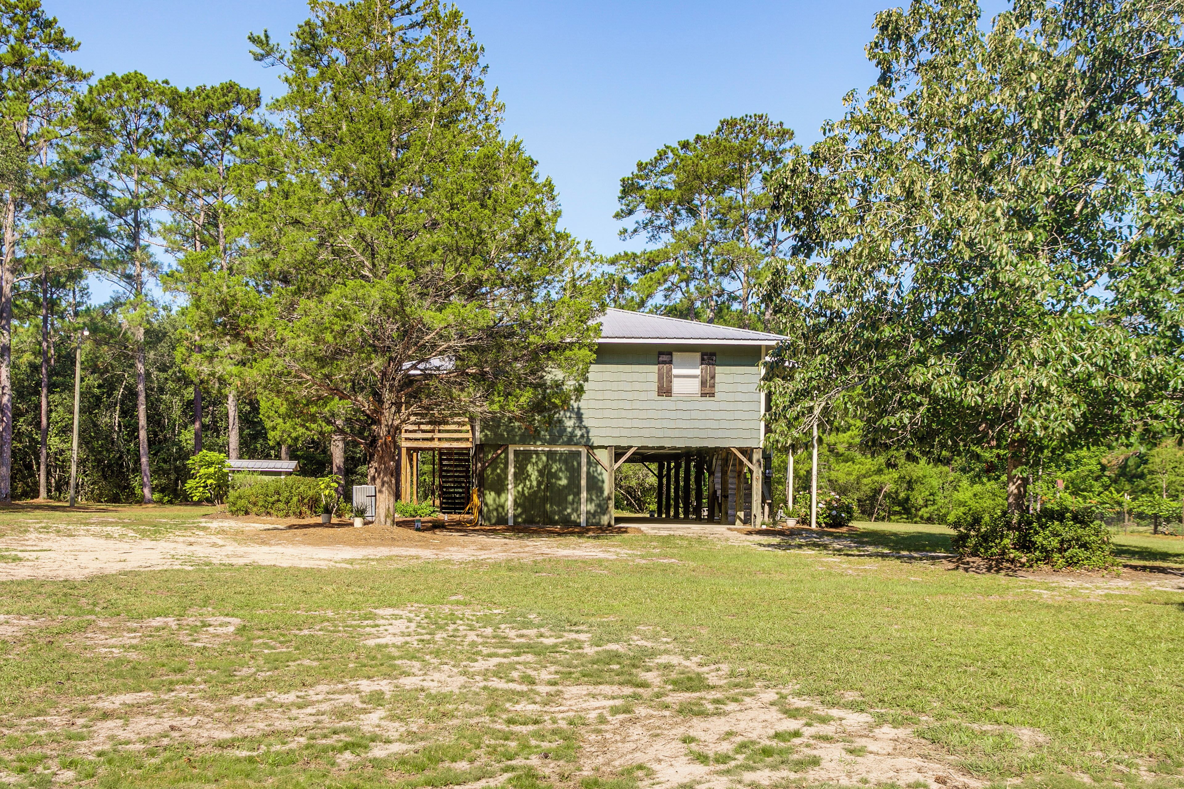 A small, single-story building with a porch, surrounded by trees and grassy area.