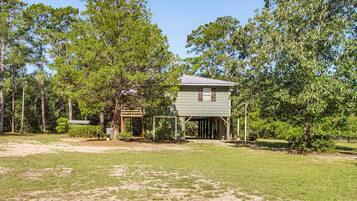 A small, single-story building with a porch, surrounded by trees and grassy area.