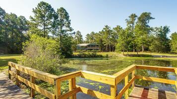 A wooden deck leading to a pond with a house in the background.