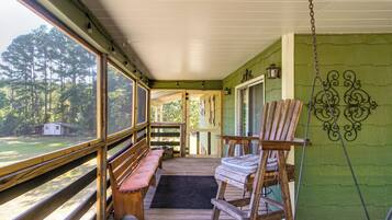 A porch with wooden benches, a suitcase, and a view of a forest.