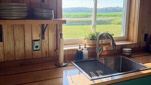 A kitchen with wooden cabinets, a stainless steel sink, and a window overlooking a green landscape.