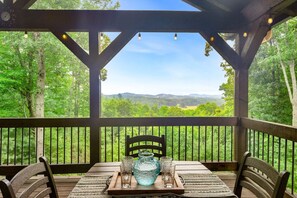 A wooden deck with a table and chairs, overlooking a forested landscape. - Mt Views, Deer Feeder, EV Chrgr, Hot Tub, Fire Pit (Morganton)