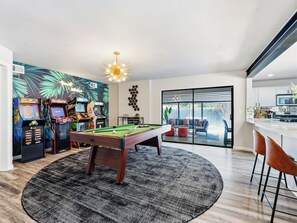 Um espaço moderno para relaxar com mesa de bilhar, jogos de fliperama e vista para um pátio externo.