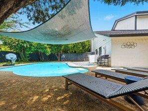 Um quintal com piscina, espreguiçadeiras, cesta de basquete e churrasqueira.