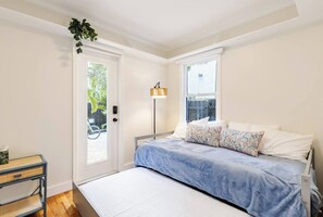 Ein Schlafzimmer mit Bett, Nachttisch, Lampe und Blick ins Freie durch ein Fenster.