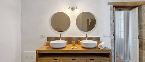 A bathroom with two round mirrors, a wooden vanity, and a stone wall.