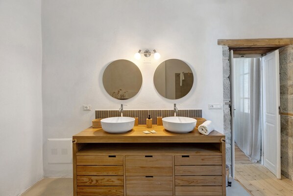Een badkamer met twee ronde spiegels, een houten wastafelmeubel en een stenen muur.
