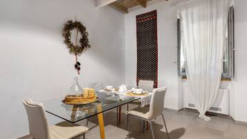 A dining area with a glass table, chairs, a decorative wreath, and a patterned wall.