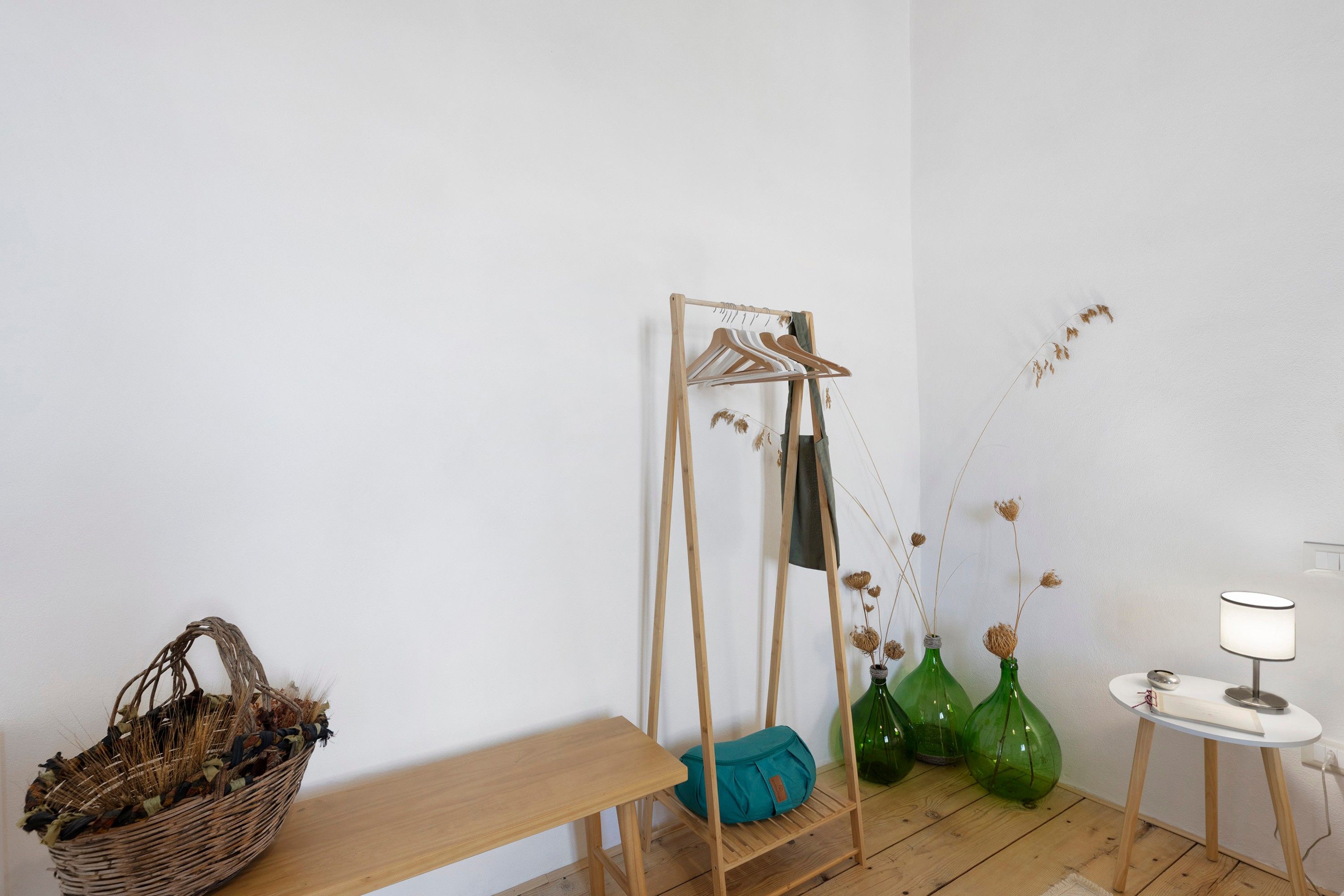 Quarto com um banco de madeira, um varal, um cesto e uma mesa com abajur.
