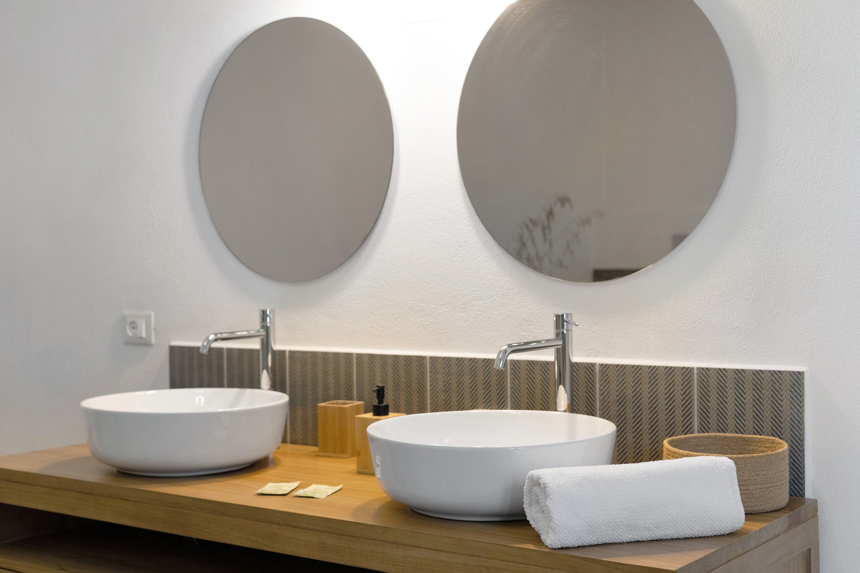 A bathroom with two large oval mirrors, a wooden vanity, and a white towel.