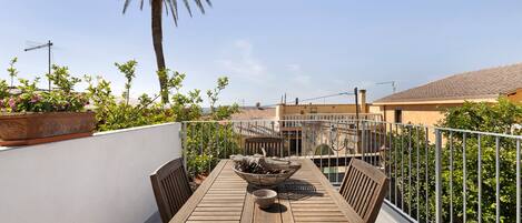 A wooden table with chairs and a bowl on a balcony with a view of buildings and a palm tree.