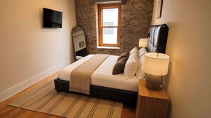 A bedroom with a bed, bedside lamp, and a television on the wall. - Market Square Steps Away | Free Parking for 2 (Knoxville)