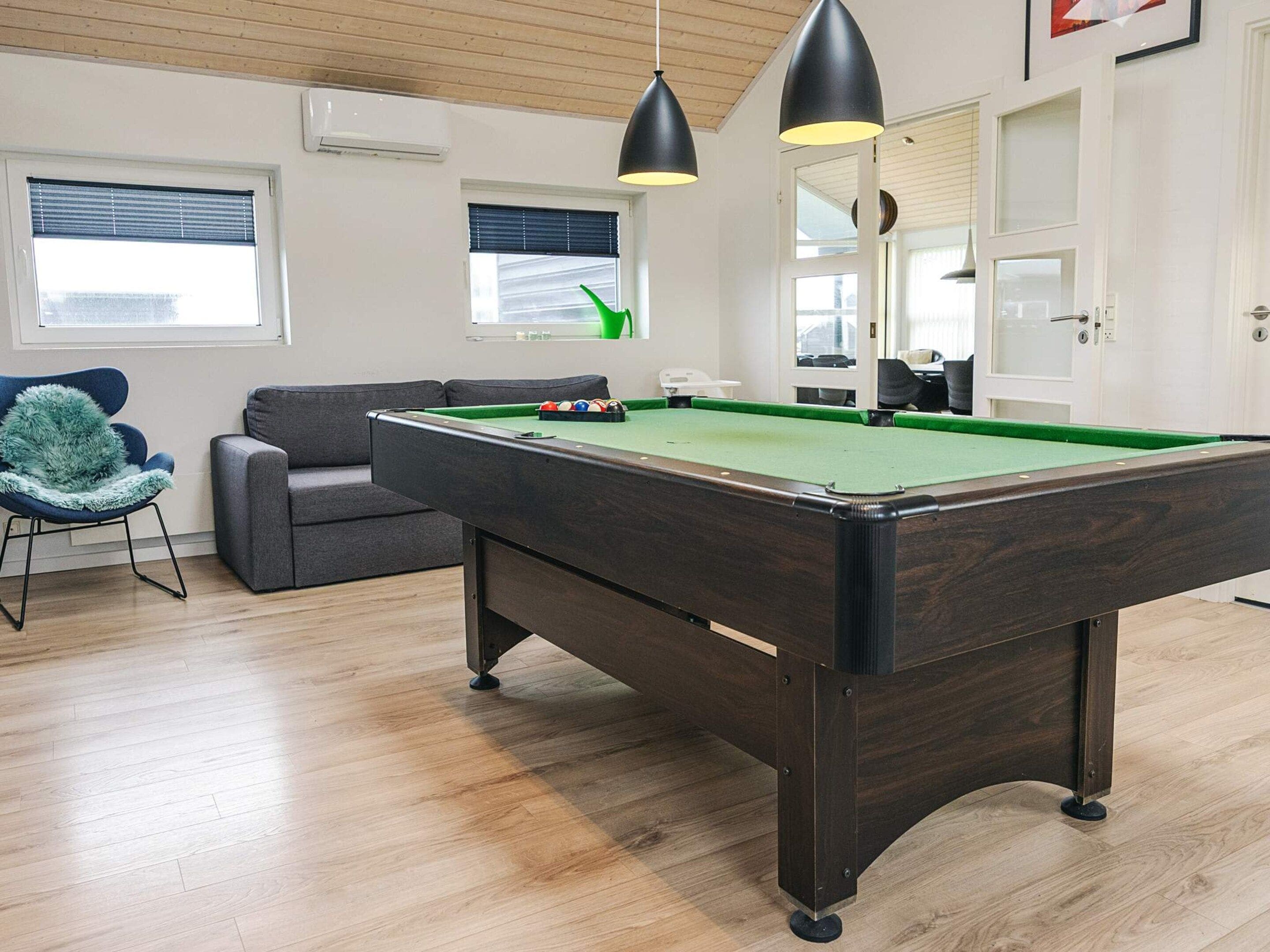 A pool table with a green felt surface, a grey sofa, and a blue chair with a fluffy cushion.