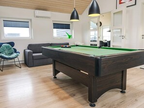 Ein Billardtisch mit grüner Spielbahn, ein graues Sofa und ein blauer Sessel mit einem flauschigen Kissen.