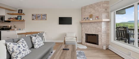 A modern living room with a fireplace, a sofa, a coffee table, and a large window offering a view of the outdoors.