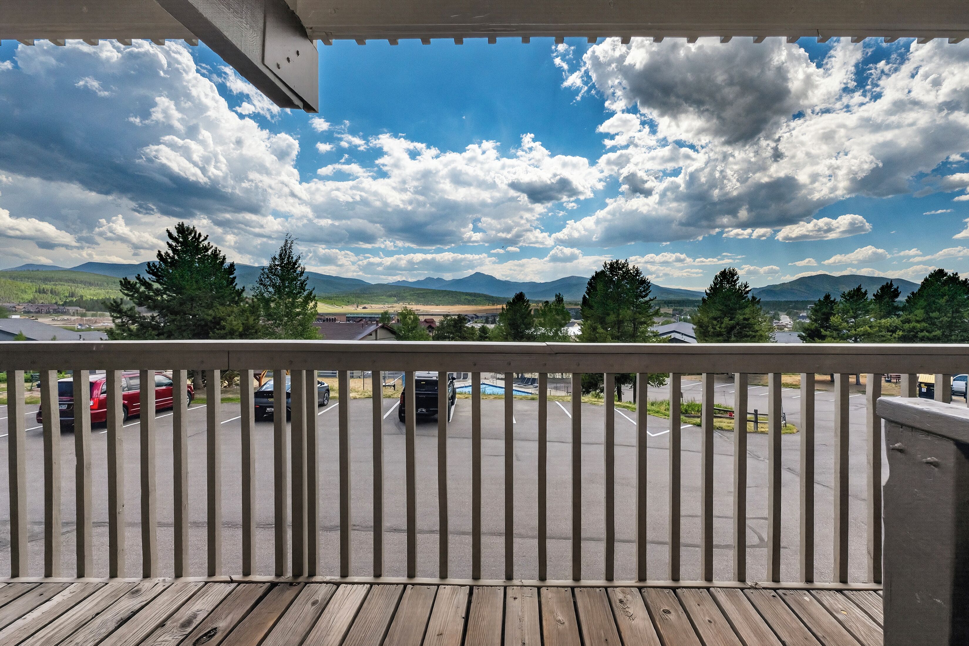 A balcony with a view of a parking lot, trees, and mountains in the distance.