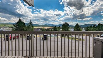 A balcony with a view of a parking lot, trees, and mountains in the distance.