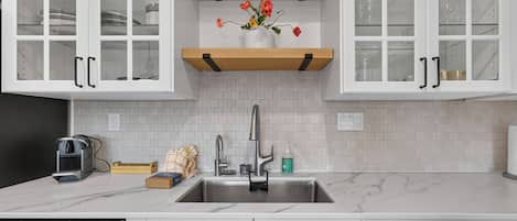A kitchen with white cabinets, a stainless steel sink, and a wooden shelf above the countertop.