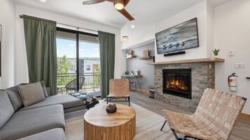 A modern living room with a fireplace, a sofa, a chair, and a television mounted above the fireplace.